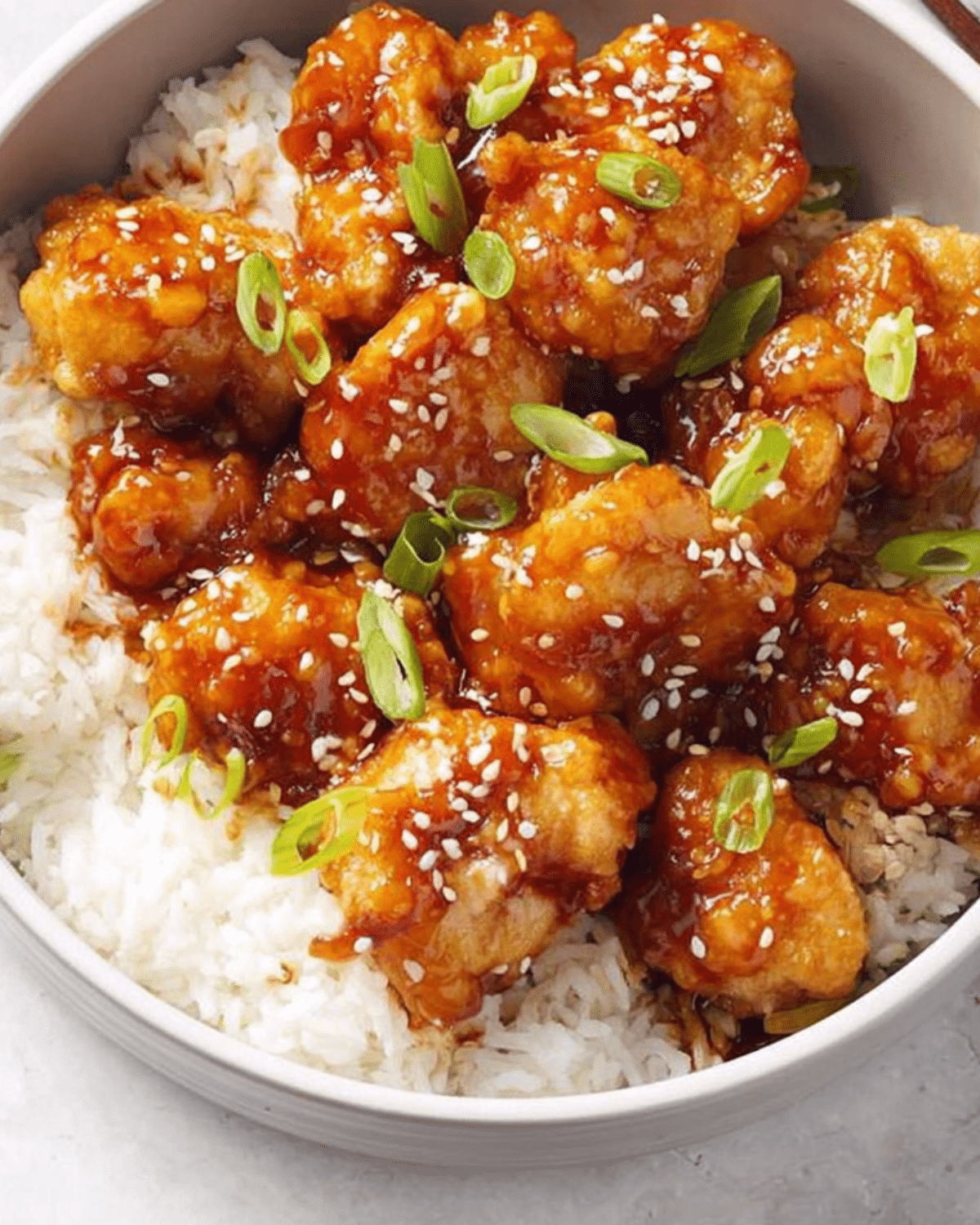 Bowl of Panda Express Orange Chicken served over white rice, topped with sesame seeds and chopped green onions.