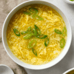 A bowl of restaurant-style egg drop soup garnished with sliced green onions.