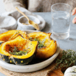 Plate of Roasted Acorn Squash wedges garnished with fresh herbs, served on a rustic wooden board.
