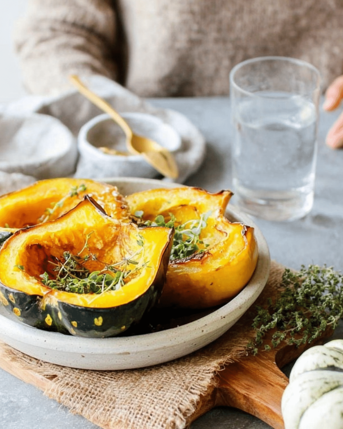 Plate of Roasted Acorn Squash wedges garnished with fresh herbs, served on a rustic wooden board.