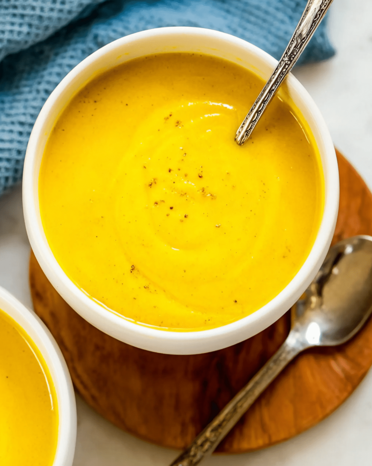 A bowl of creamy Roasted Butternut Squash Soup garnished with cracked pepper and served with a spoon.