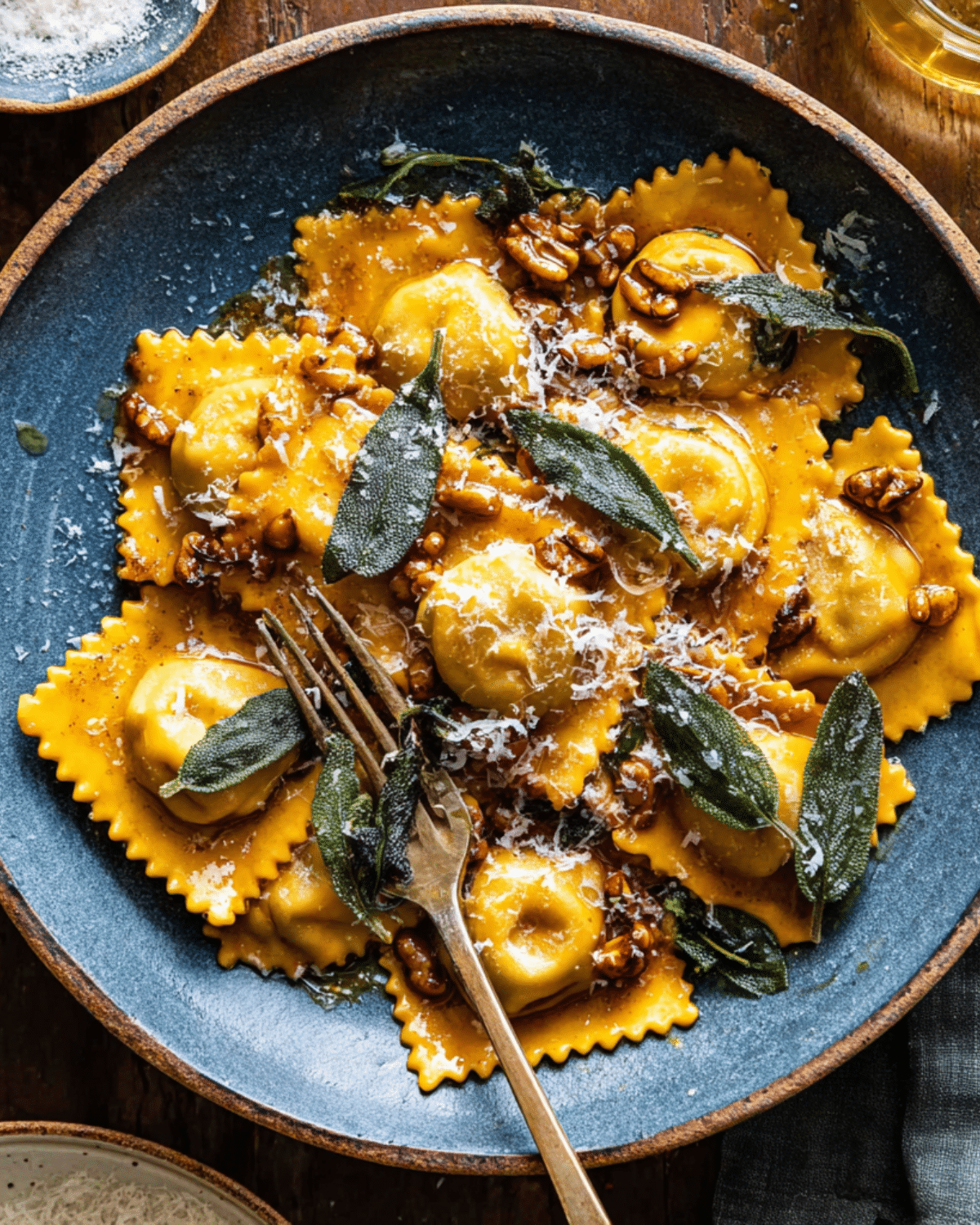 Plate of Sage Butter Pumpkin Cheese Ravioli topped with crispy sage leaves, chopped walnuts, and grated Parmesan cheese.