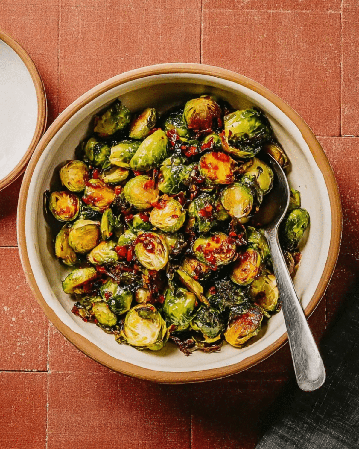 Sweet Chili Brussel Sprouts served in a beige bowl, coated in a glossy sweet and spicy sauce with bits of red chili.