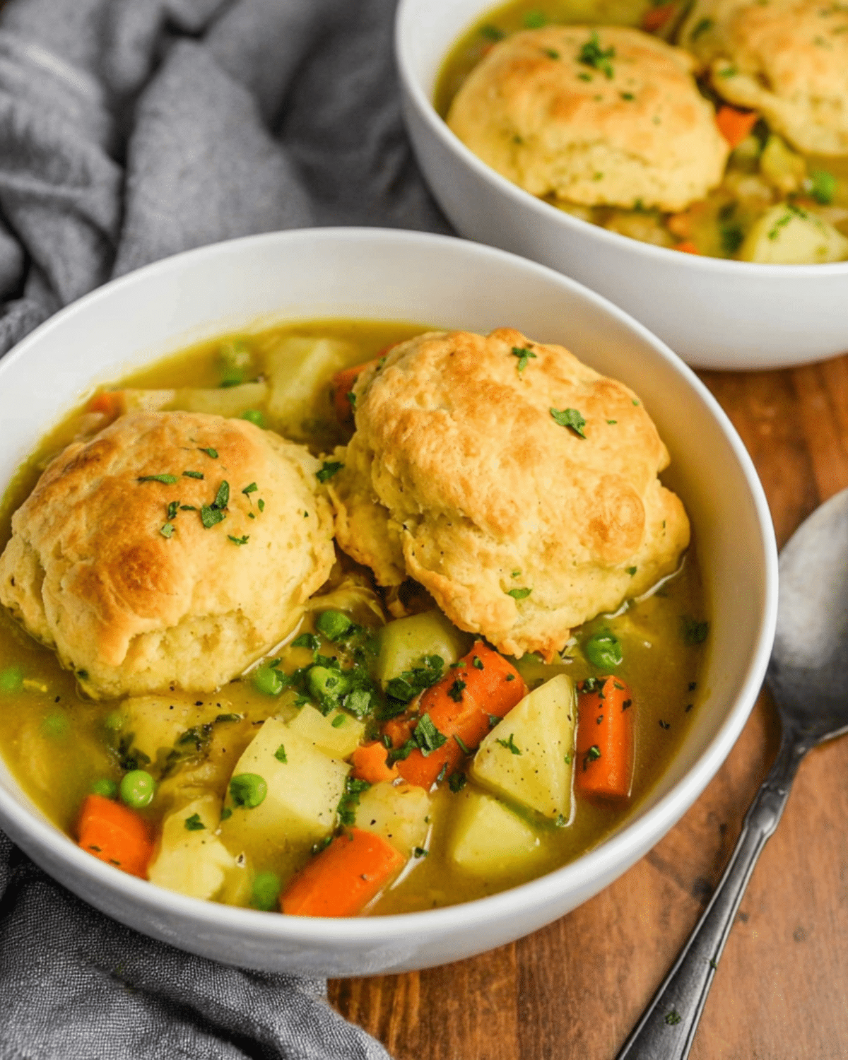 A bowl of veggie pot pie soup topped with two golden, fluffy biscuits and filled with carrots, potatoes, peas, and herbs.