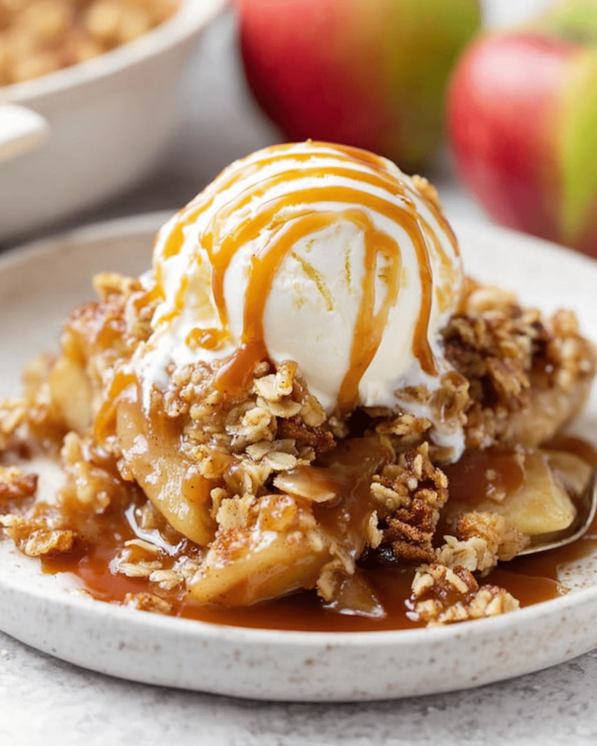Warm caramel apple crisp topped with vanilla ice cream and drizzled with rich caramel sauce, served on a ceramic plate.
