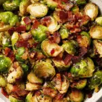Bowl of roasted Brussels sprouts with crispy bacon pieces, lightly caramelized and seasoned.