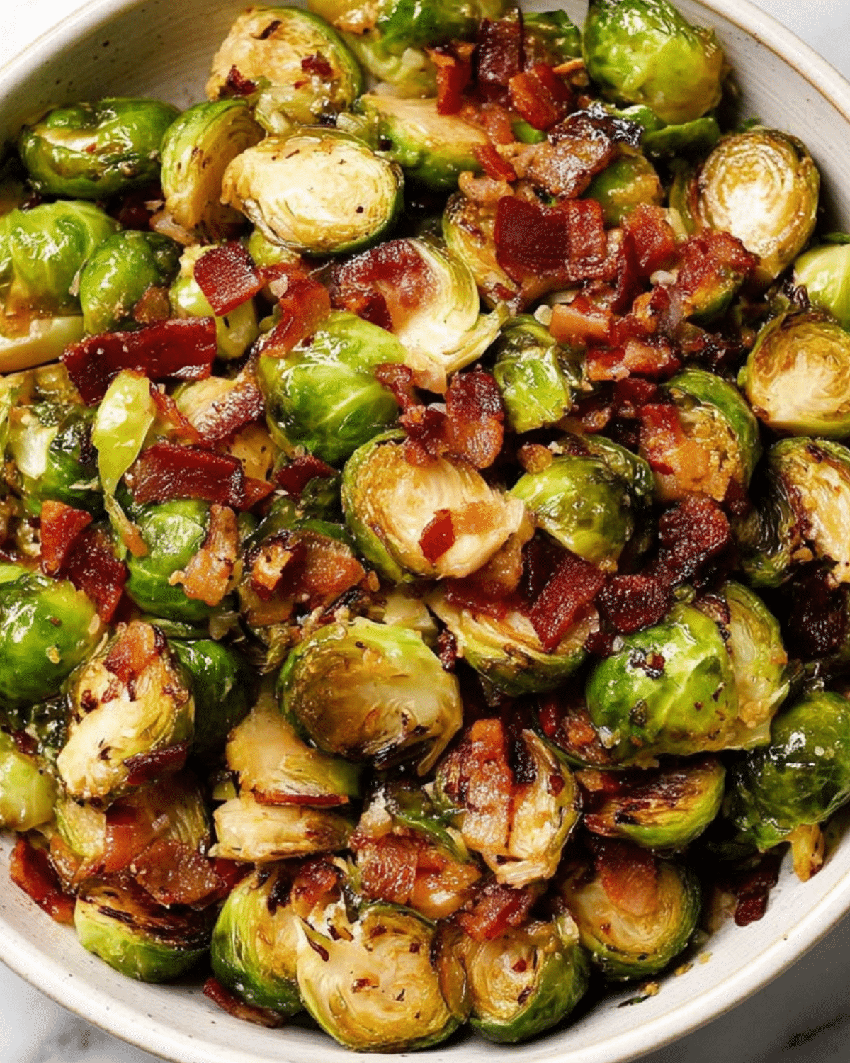 Bowl of roasted Brussels sprouts with crispy bacon pieces, lightly caramelized and seasoned.