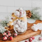 Glass jar filled with candied cranberries coated in sugar, surrounded by festive holiday decor.