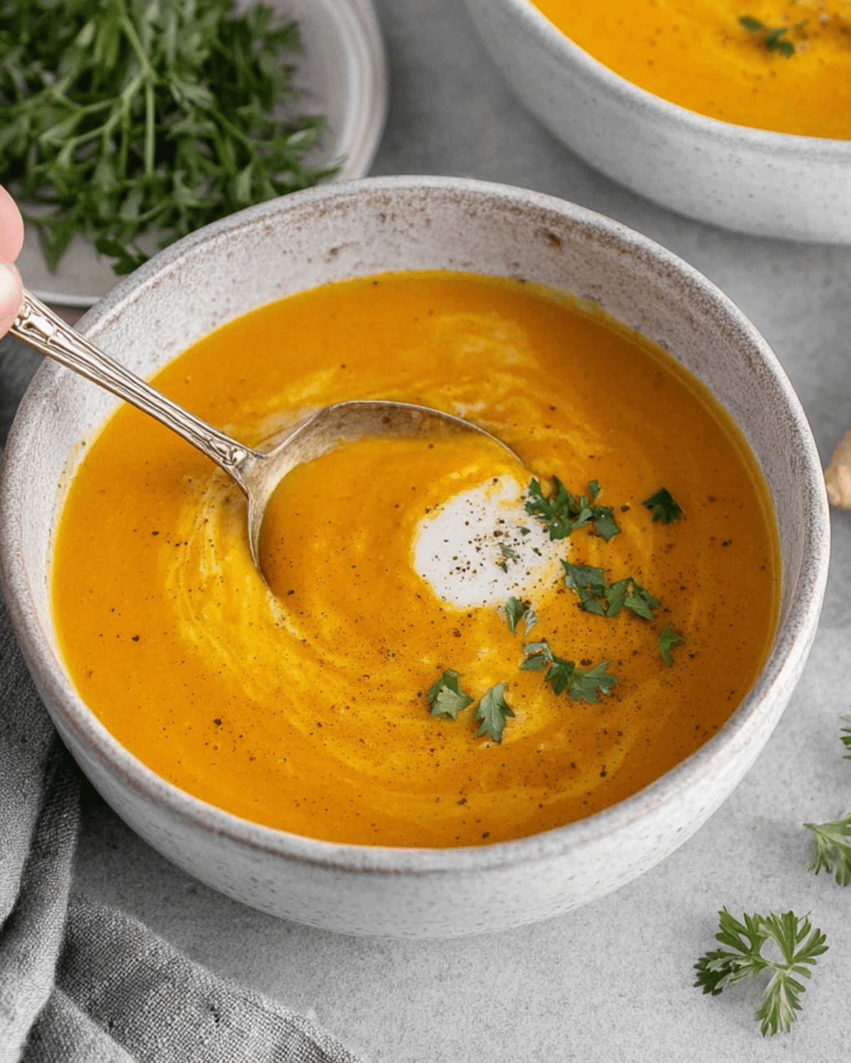 Bowl of creamy Carrot Ginger Soup garnished with herbs and a swirl of cream