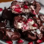 A plate of chocolate covered pomegranate yogurt clusters, broken open to reveal juicy pomegranate seeds and creamy yogurt filling inside the rich chocolate shell.