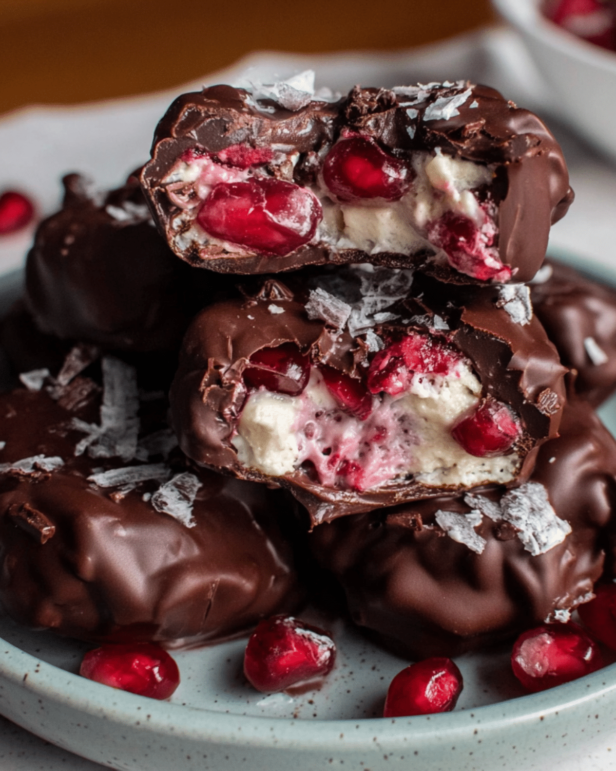 A plate of chocolate covered pomegranate yogurt clusters, broken open to reveal juicy pomegranate seeds and creamy yogurt filling inside the rich chocolate shell.