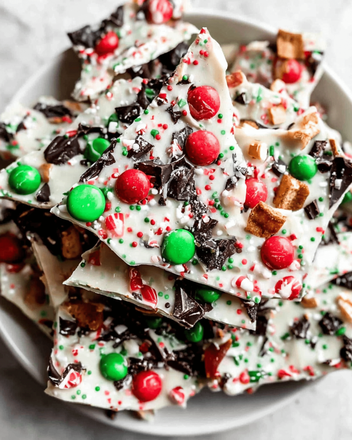 Colorful Christmas candy bark topped with red and green candies, crushed peppermint, sprinkles, and chocolate chunks.