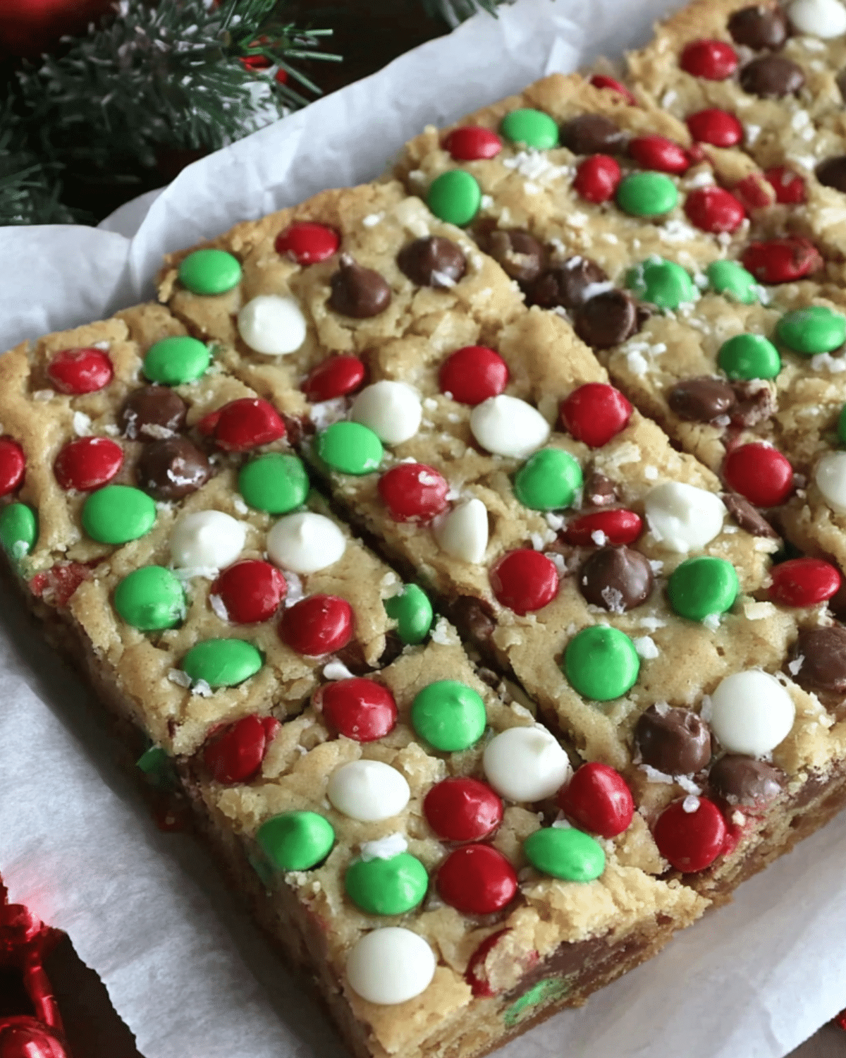 Christmas cookie bars topped with red, green, white candy-coated chocolates and chocolate chips, cut into festive squares.