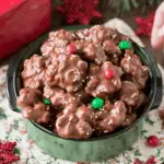 Bowl of Christmas Crock Pot Candy clusters coated in chocolate, topped with festive red and green candies and sprinkles.