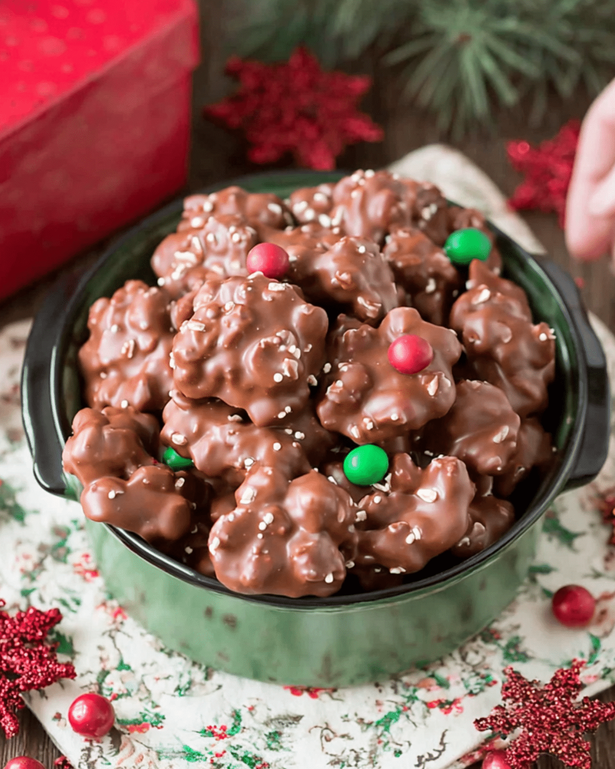 Bowl of Christmas Crock Pot Candy clusters coated in chocolate, topped with festive red and green candies and sprinkles.