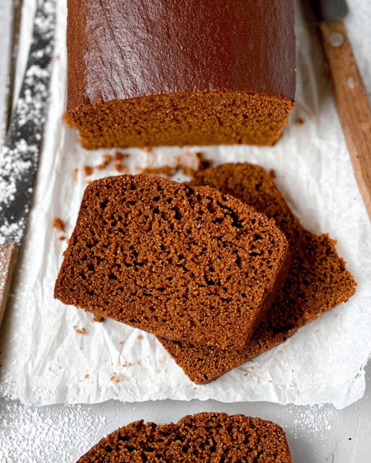 Slices of classic gingerbread loaf on parchment paper, showing the moist and spiced interior of the baked loaf.