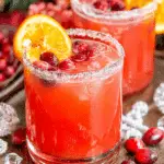 Glass of Cranberry Christmas Cocktail garnished with cranberries and an orange slice, rimmed with sugar.