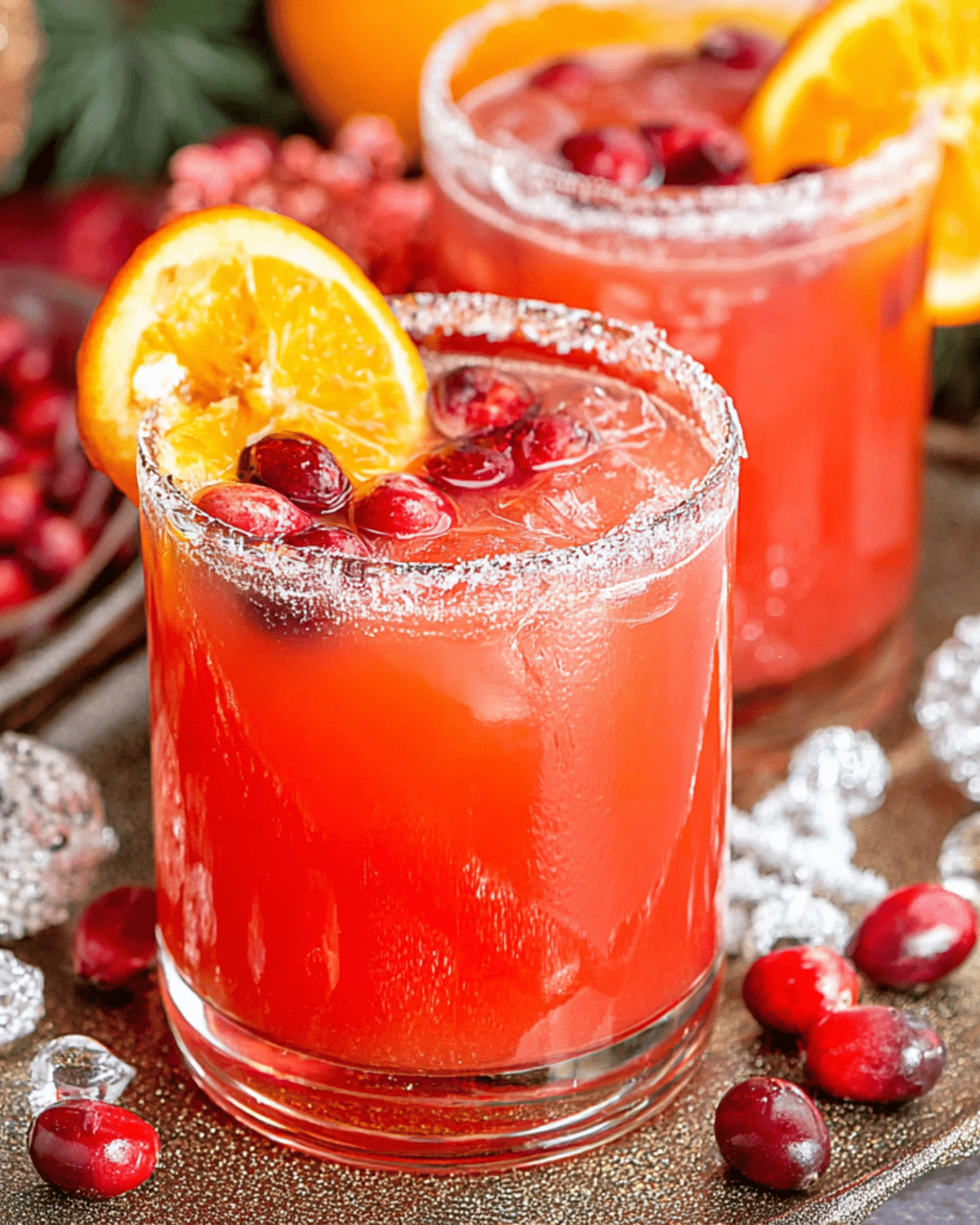 Glass of Cranberry Christmas Cocktail garnished with cranberries and an orange slice, rimmed with sugar.