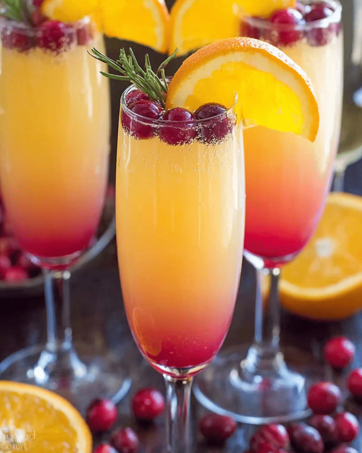 Flutes of Cranberry Orange Mimosa garnished with cranberries, orange slices, and rosemary sprigs.