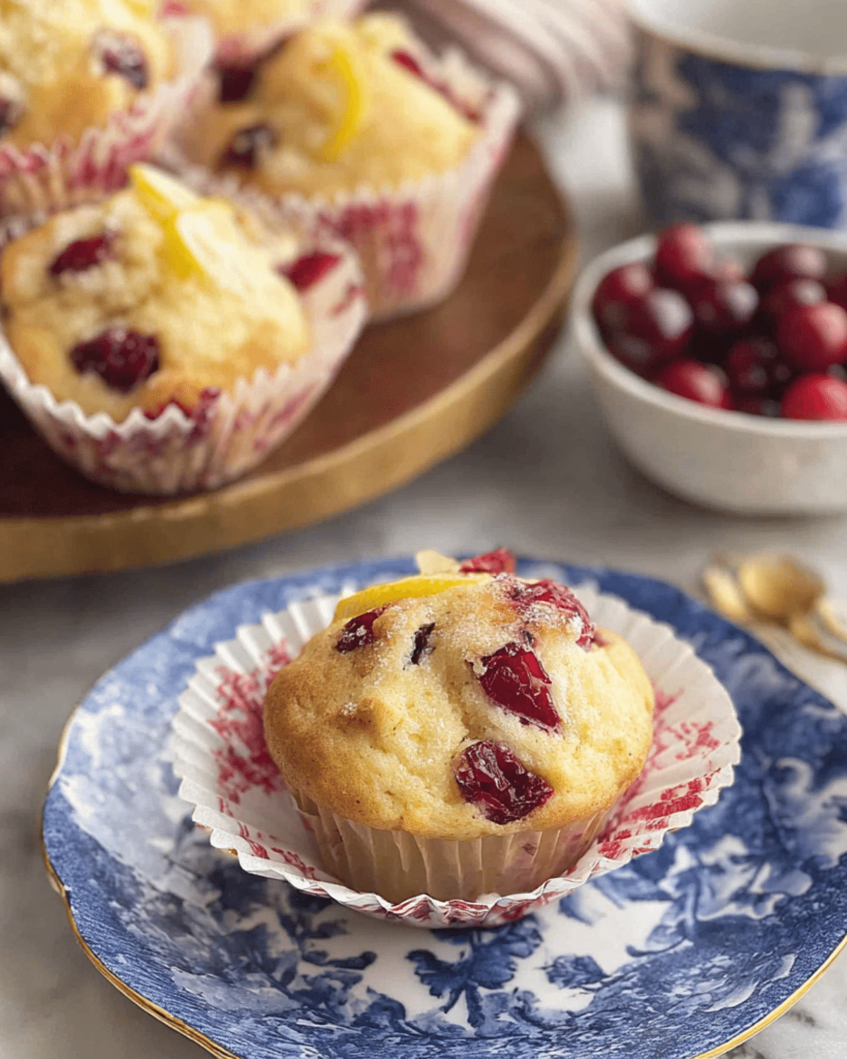 A freshly baked Cranberry Orange Muffin on a decorative plate, topped with sugared cranberries and orange zest.