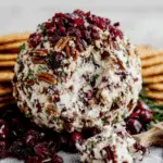 Cranberry Pecan Cheese Ball covered in chopped pecans, cranberries, and herbs, served with crackers.