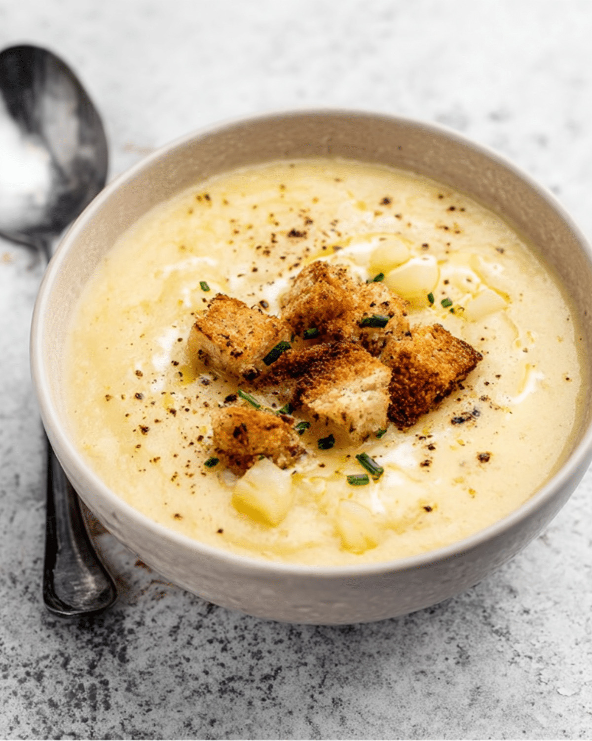 Bowl of creamy roasted garlic potato soup topped with croutons, chopped chives, and cracked black pepper.