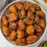 Bowl of Crispy Honey Chicken Bites topped with sesame seeds and chopped green onions.