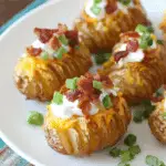 Crispy loaded Hasselback potato bites topped with cheese, sour cream, bacon, and green onions on a white plate.