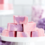 Stacked pieces of dreamy cotton candy fudge with pink and purple swirls displayed on a white cake stand.
