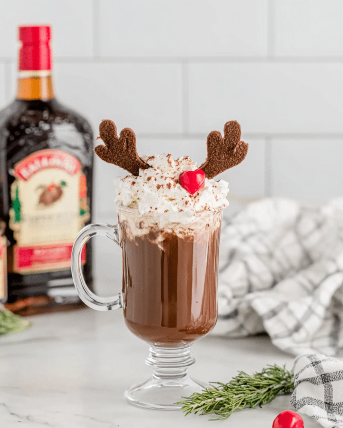 Festive Drunken Rudolph cocktail topped with whipped cream, chocolate antlers, and a cherry nose in a clear glass mug.