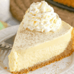 Slice of eggnog cheesecake on a white plate, topped with whipped cream and sprinkled with nutmeg.