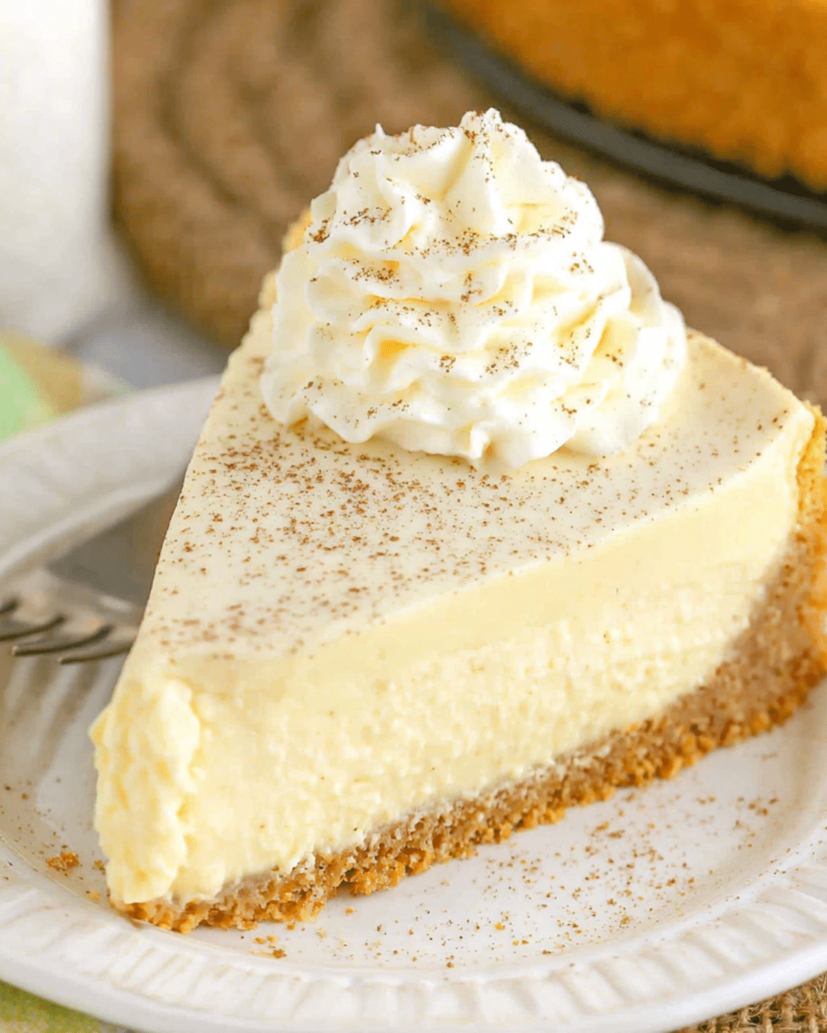 Slice of eggnog cheesecake on a white plate, topped with whipped cream and sprinkled with nutmeg.