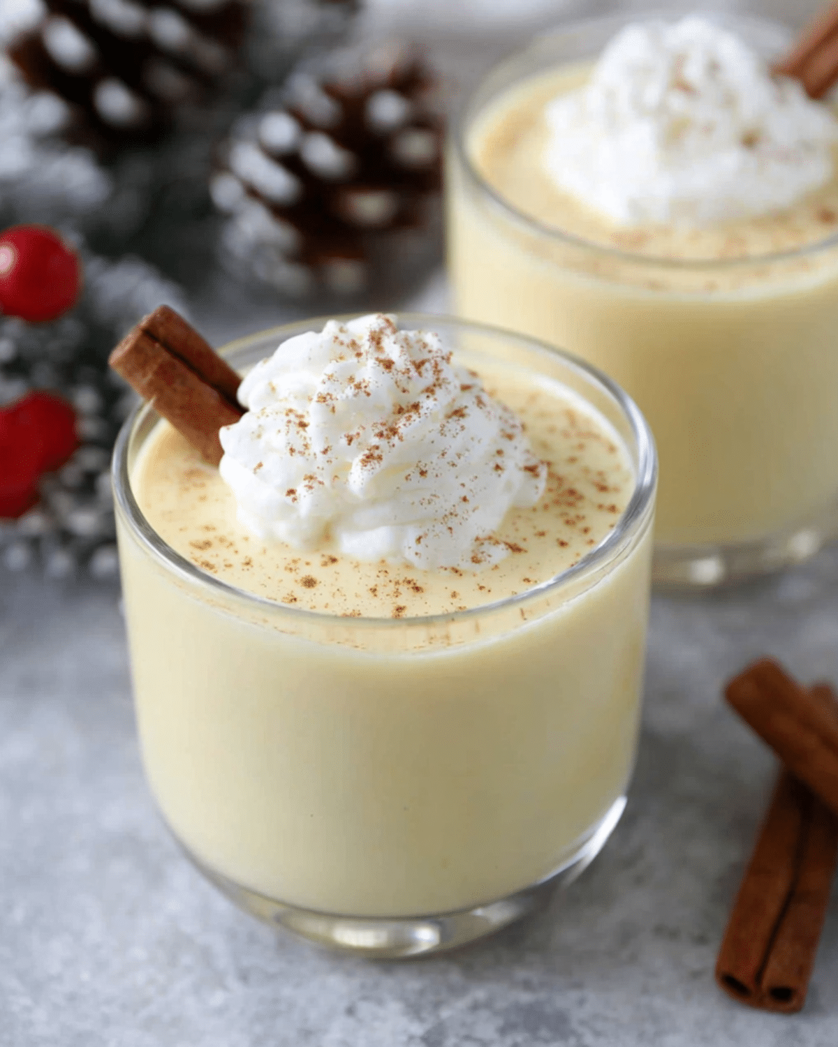 Glass of homemade Eggnog topped with whipped cream, sprinkled with nutmeg, and garnished with a cinnamon stick.