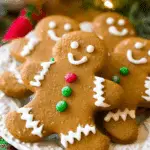 A festive plate of gingerbread men cookies decorated with white icing and colorful candy buttons, set against a holiday background.