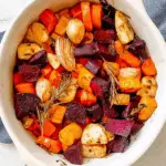 Baking dish filled with honey roasted winter vegetables, including carrots, beets, parsnips, onions, and rosemary.