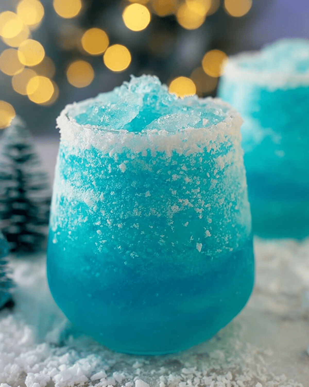 Frosted glass of icy blue Jack Frost Cocktail with a coconut-rimmed edge surrounded by snow-like decor.