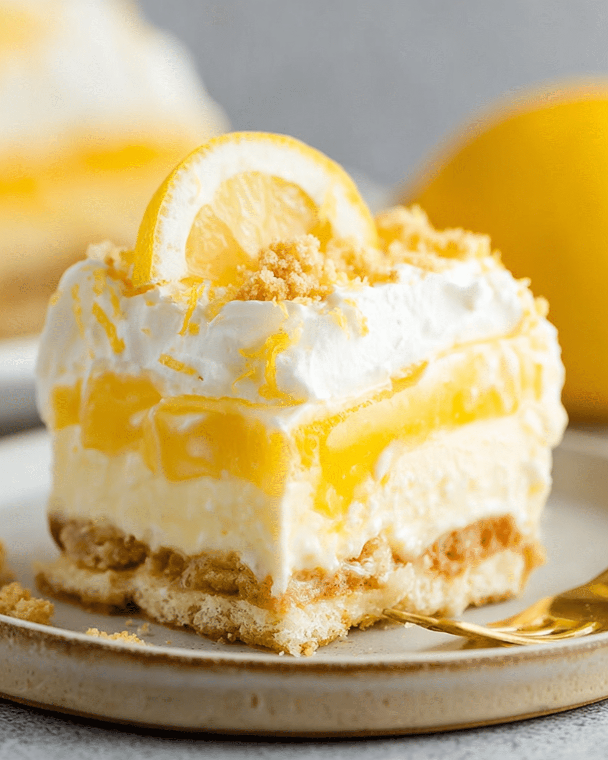 A slice of lemon lush dessert with creamy layers, lemon filling, whipped topping, and a lemon wedge on a ceramic plate.