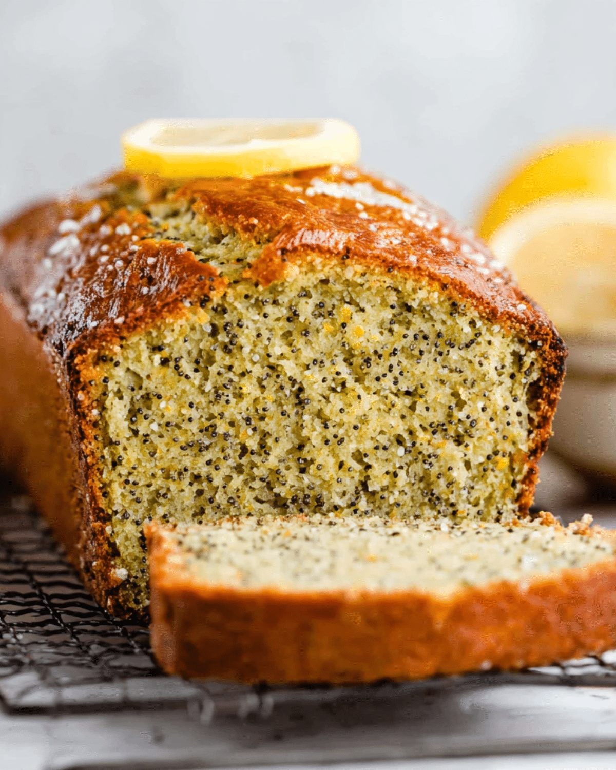 Loaf of Lemon Poppy Seed Bread with a golden crust, sliced to reveal its moist, speckled interior, topped with a lemon slice.