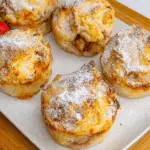 Golden mini apple pies with puff pastry, dusted with powdered sugar and served on a white platter.