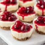 Mini Cherry Cheesecakes topped with vibrant cherry pie filling, sitting on a graham cracker crust.