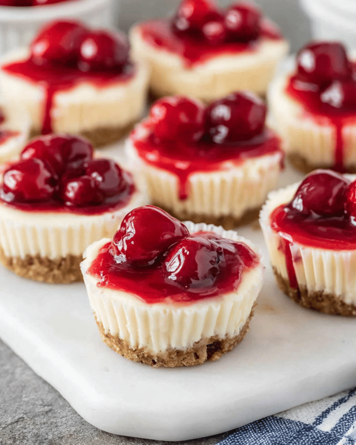 Mini Cherry Cheesecakes topped with vibrant cherry pie filling, sitting on a graham cracker crust.