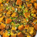 Golden mushroom and herb stuffing with crispy bread cubes, sautéed mushrooms, green onions, and fresh herbs in a white baking dish.