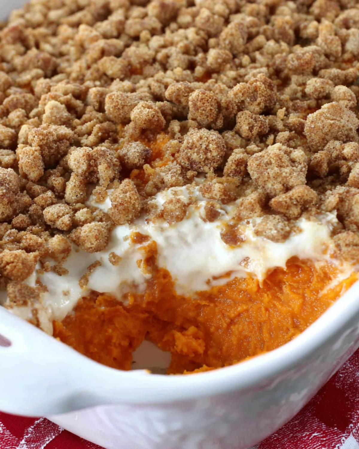 A white casserole dish filled with old-fashioned sweet potato casserole, topped with a golden brown pecan crumble and a creamy layer, with a serving scooped out.