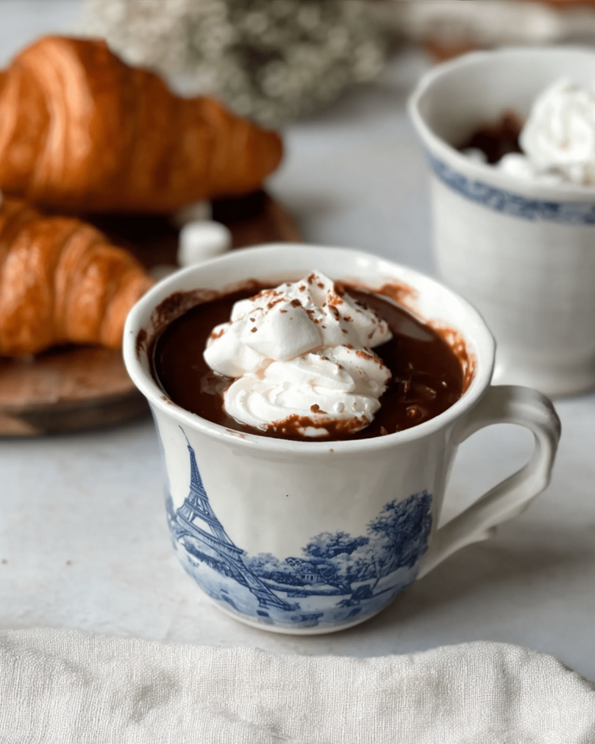 Paris Hot Chocolate served in a white mug with blue Eiffel Tower design, topped with whipped cream and marshmallows.