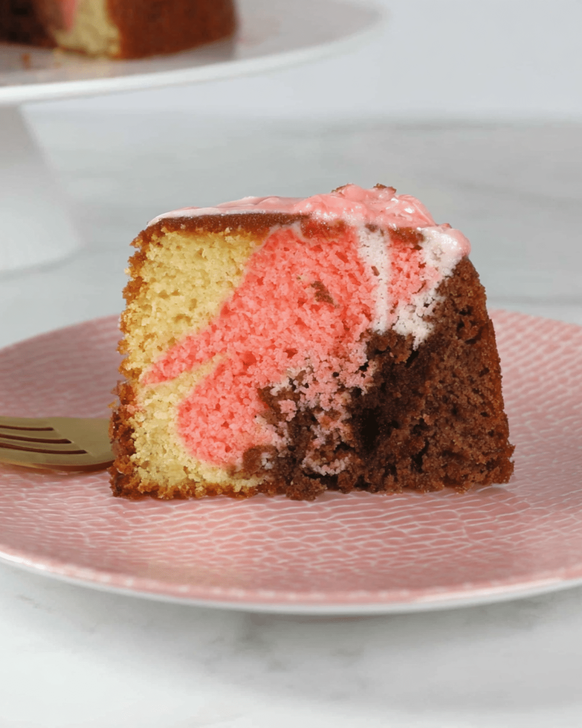 A slice of Pink Marble Cake with vanilla, chocolate, and pink swirls served on a pink plate.