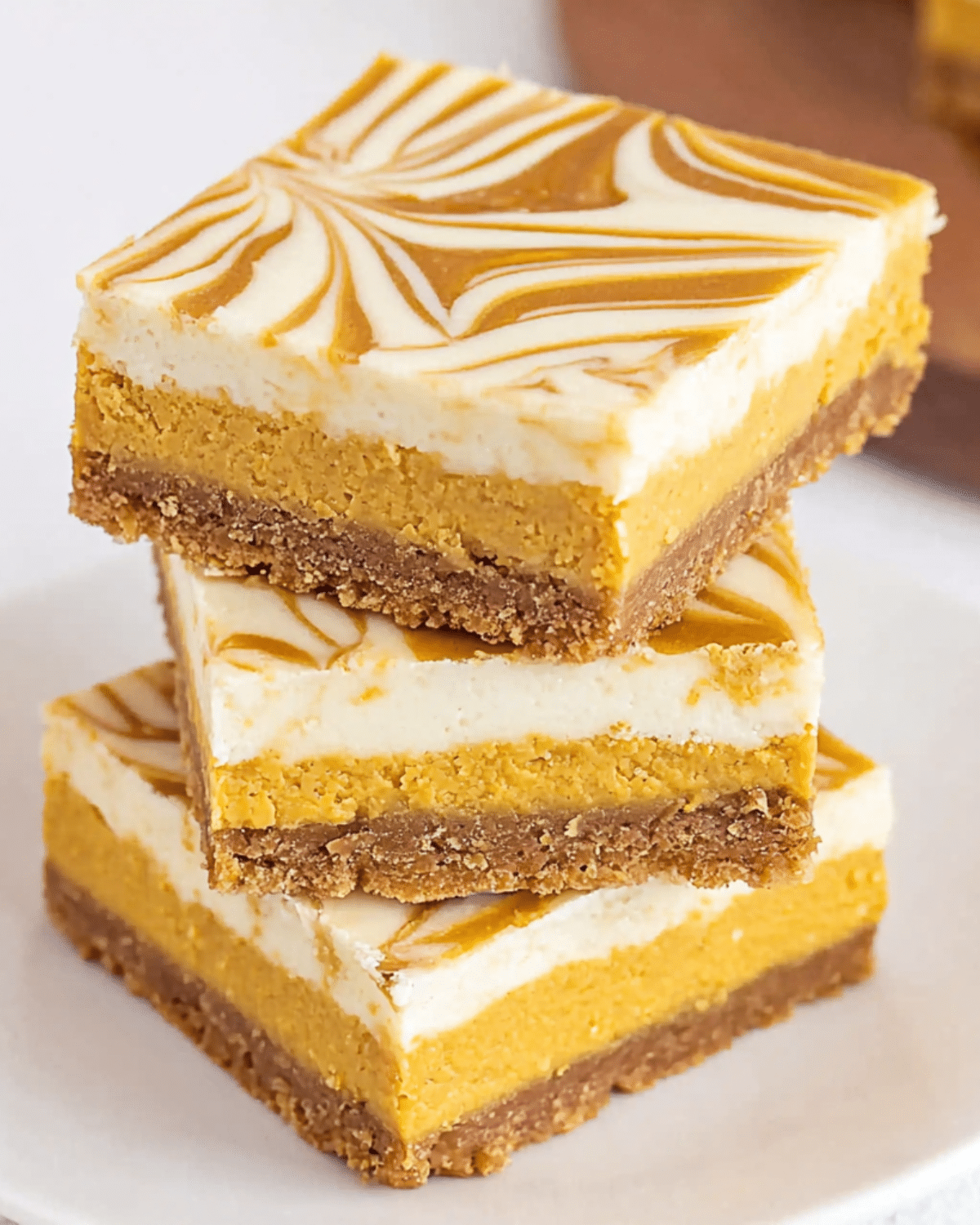 Stack of Pumpkin Spice Cheesecake Bars with a swirled top and graham cracker crust.