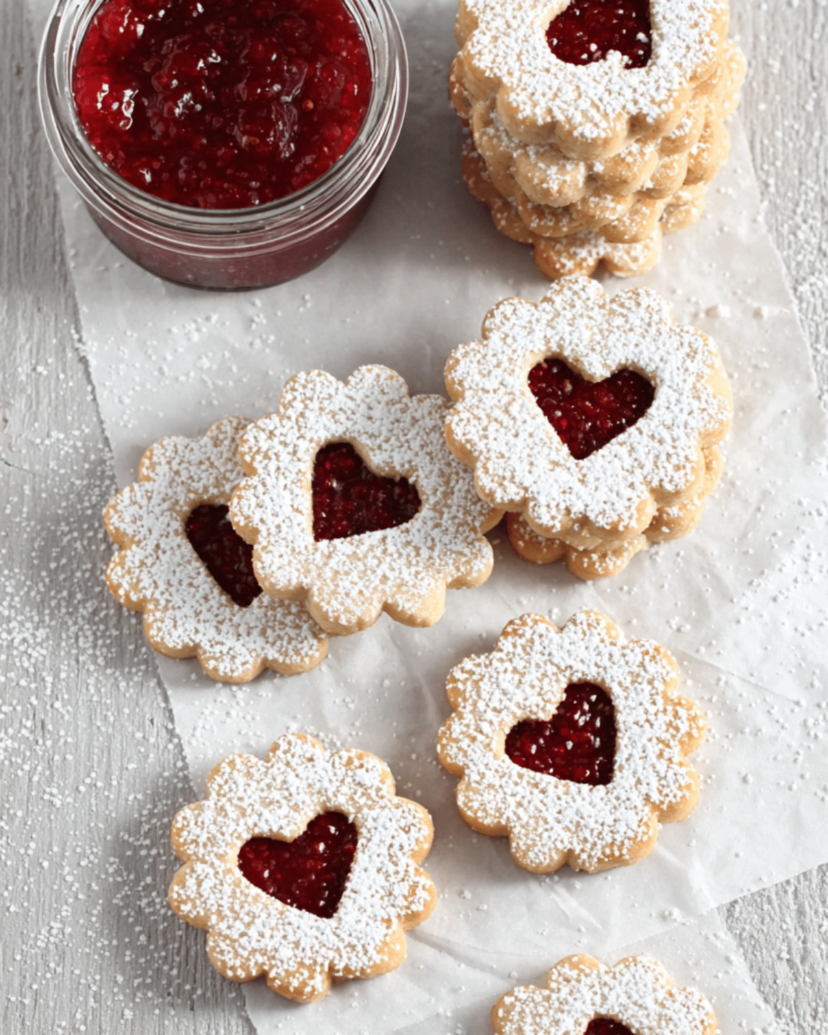 Raspberry Linzer Cookies with heart-shaped cutouts and powdered sugar, filled with raspberry jam.