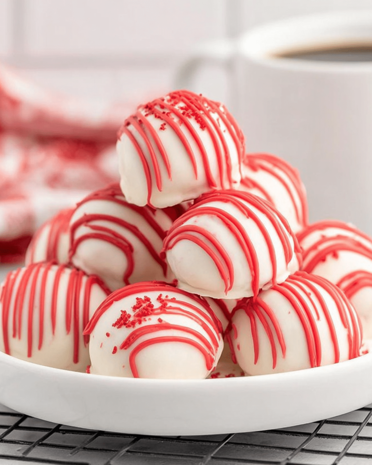 A stack of Red Velvet Cheesecake Bites covered in white chocolate and drizzled with red icing on a white plate.