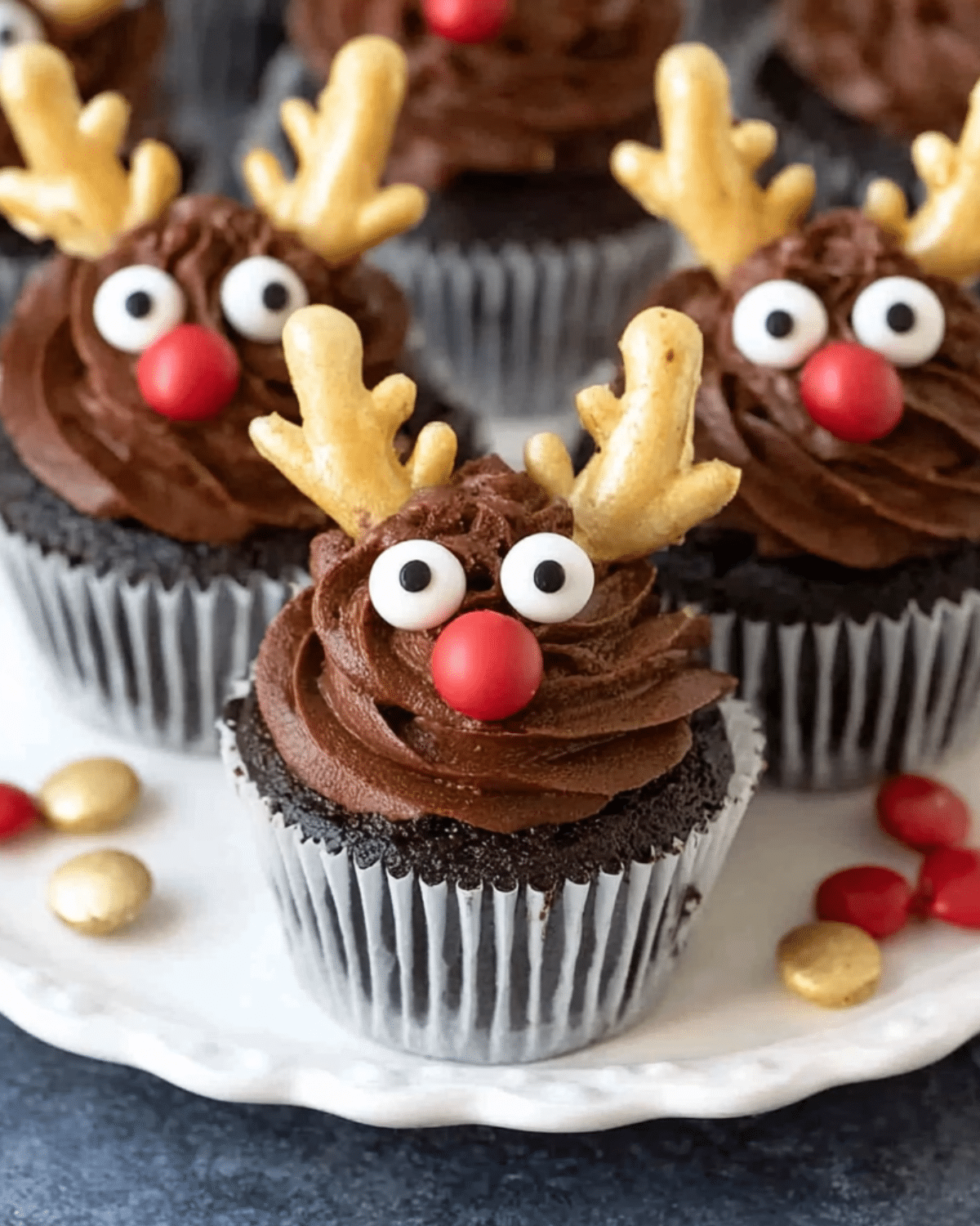 Chocolate Reindeer Cupcakes decorated with candy eyes, red noses, and golden antlers.