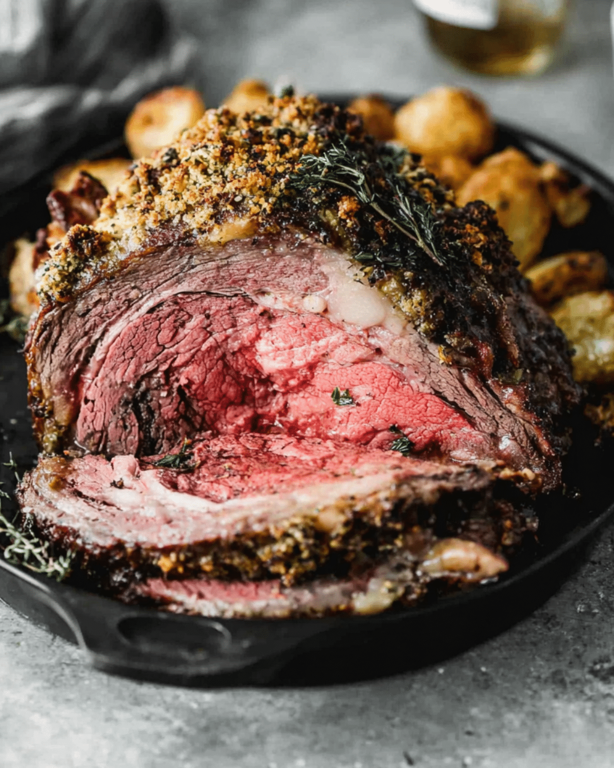 Sliced roast prime rib with a crispy herb crust, served in a cast iron skillet with roasted potatoes.